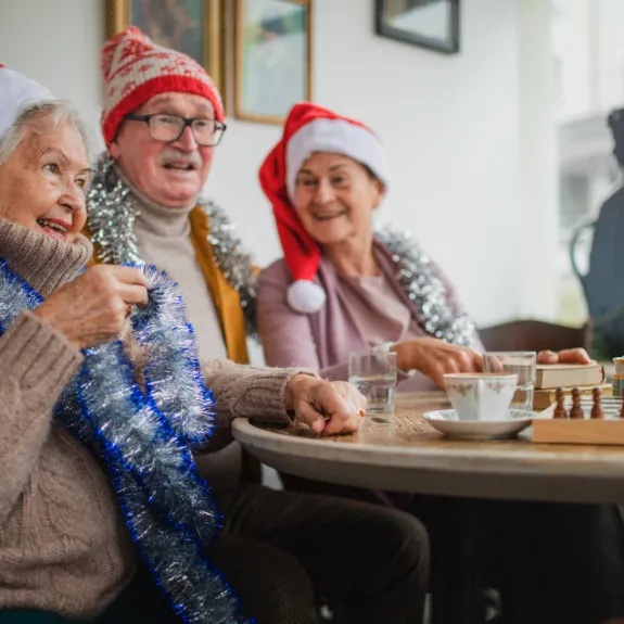 Mehrere alte Personen haben eine Weihnachtsmütze auf und sitzen gemeinsam an einem Tisch und trinken dort Tee.