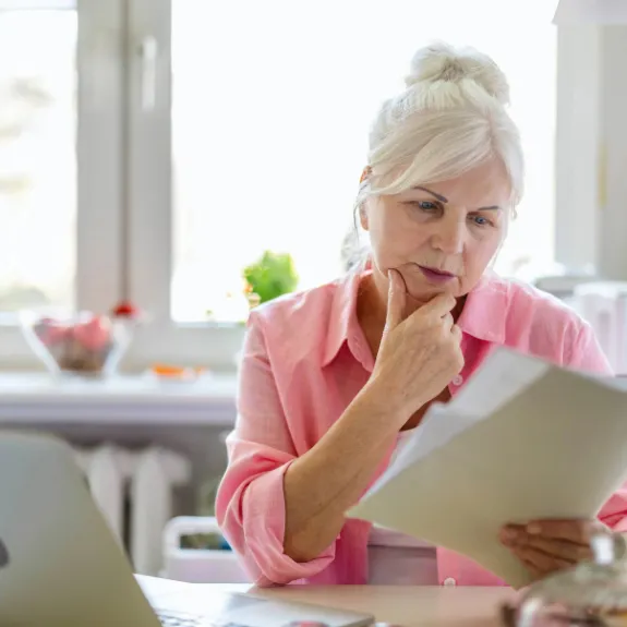 Seniorin verfasst Vollmacht mit Laptop und Dokumenten am Kuechentisch bei sich zu Hause