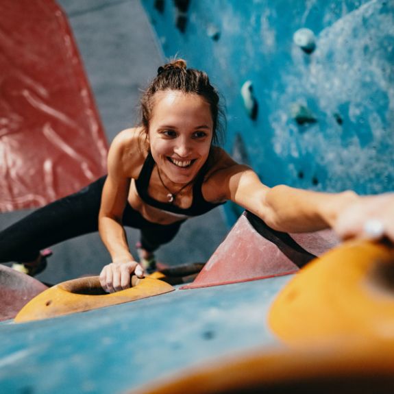 Frau klettert eine Indoor-Kletterwand hoch.