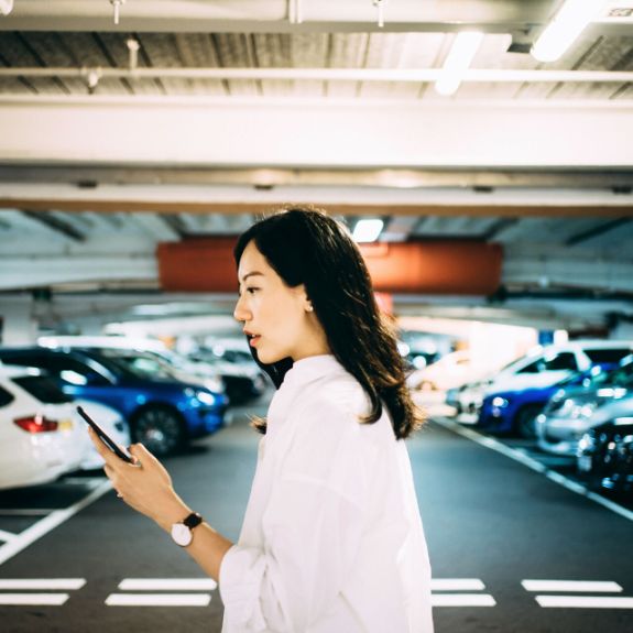 Junge Frau steht in einer Tiefgarage und schaut auf ihr Handy.