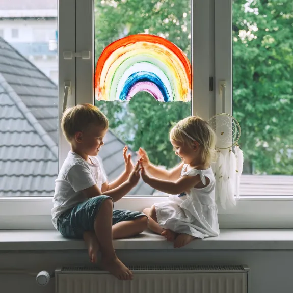 Zwei Kleinkinder sitzen auf der Fensterbank und klatschen sich in die Hände.