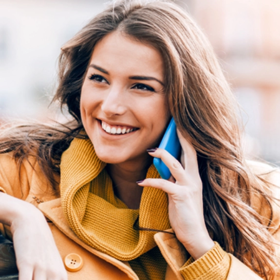 Lächelnde Frau in gelbem Pullover telefoniert mit blauem Smartphone