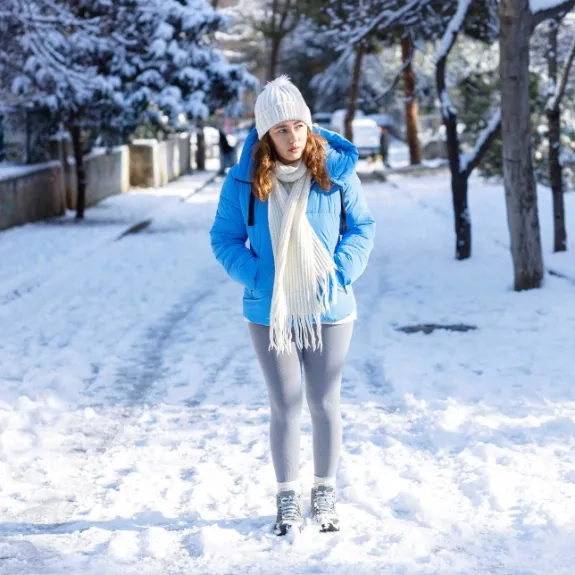 Eine Frau läuft bei Schnee und Glatteis vorsichtig auf dem Gehweg.