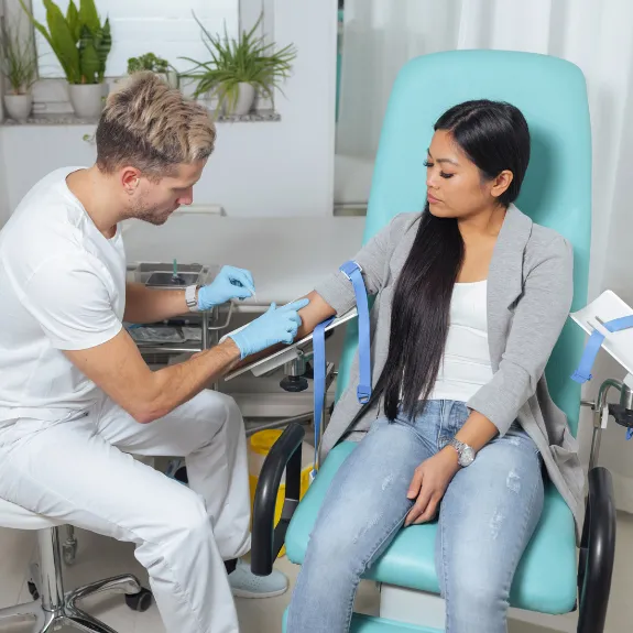 Ein Krankenpfleger nimmt einer jungen Frau Blut ab für das große Blutbild.