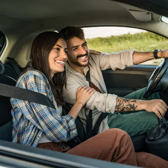 Ein Mann und eine Frau fahren im Auto. Sie lachen und sie berührt ihn am Arm.