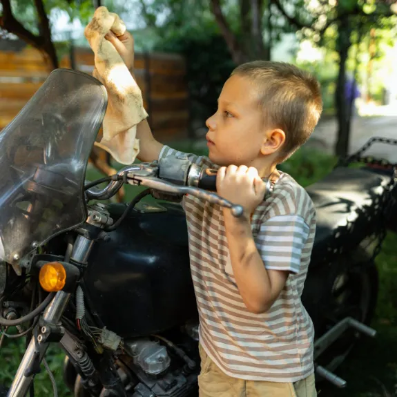 Motorrad waschen: Ein Kind reinigt ein Motorrad mit einem Tuch.