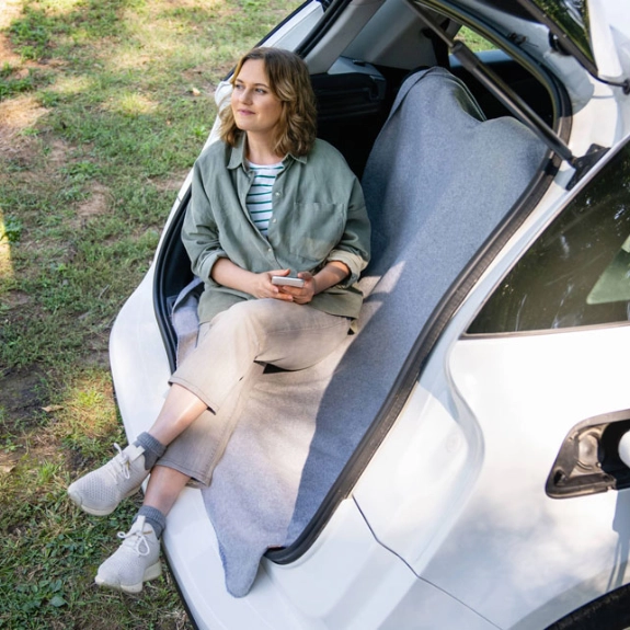 Eine Frau lädt ihr Elektroauto während sie im Kofferraum sitzt und wartet.