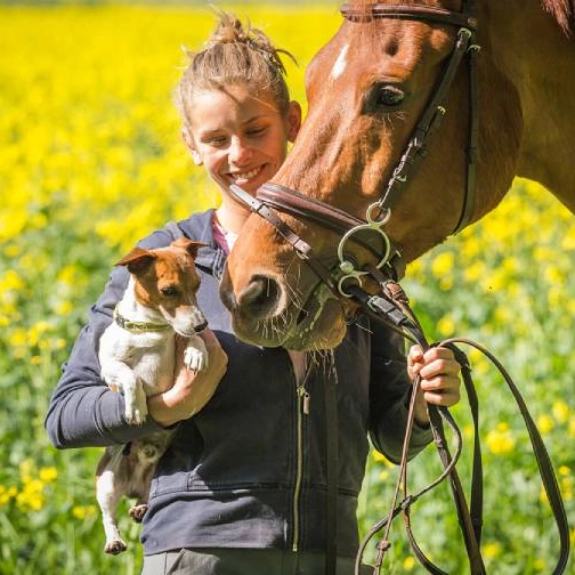 Eine Frau mit einem Hund auf dem Arm und einem Pferd.
