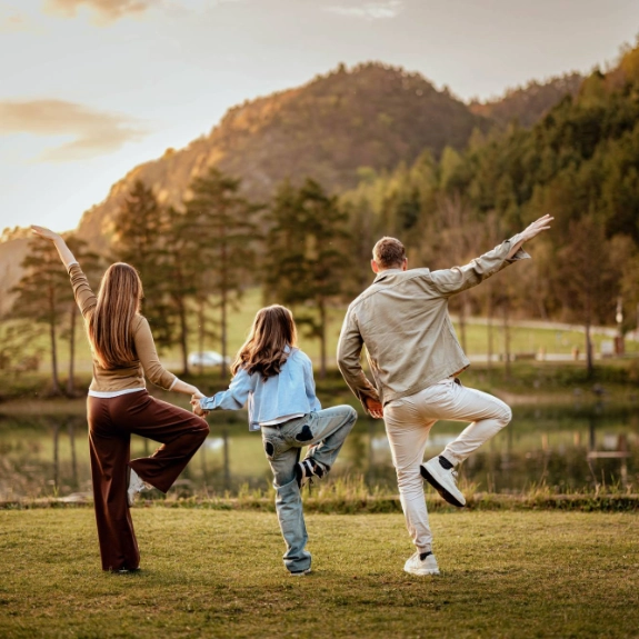 Familie macht Yoga im Freien, Mutter und Vater und Kind halten sich an den Händen.