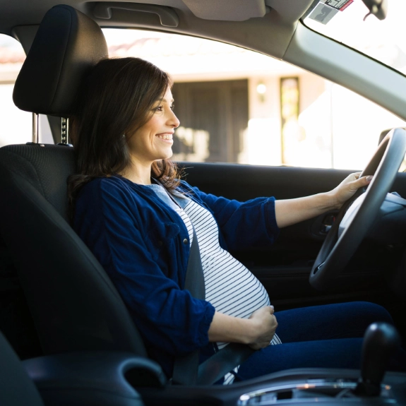 Eine werdende Mutter sitzt mit Babybauch am Steuer als Symbol für das Autofahren in der Schwangerschaft.