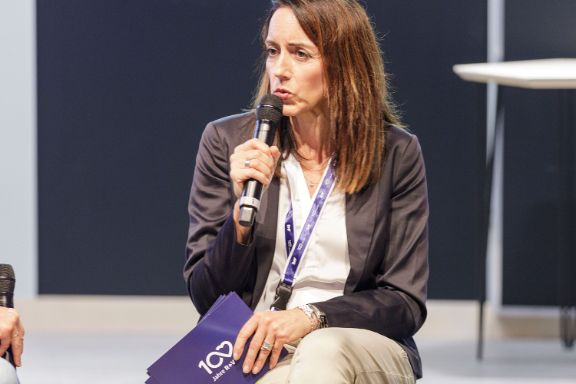 Katja Streck sitzt auf einem Stuhl, hat ein Mikrophon in der Hand und hält einen Vortrag