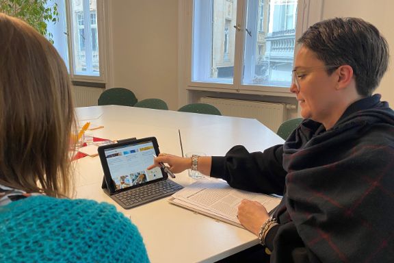 Zwei Frauen sitzen an einem Schreibtisch und betrachten eine Website auf einem Laptop