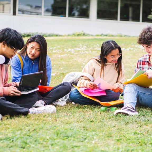 Junge Menschen sitzen auf einer Wiese auf dem Campus und lernen.