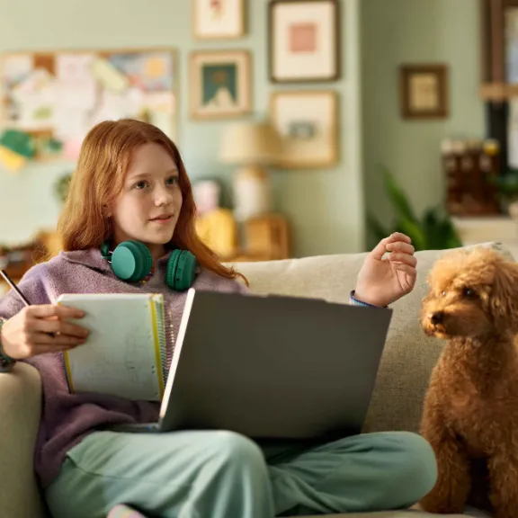 Ein junges Mädchen sitzt auf dem Sofa und erkundigt sich mit ihrem Computer über eine Berufsunfähigkeitsversicherung für Schüler.