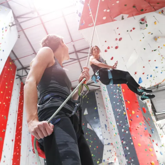 Zwei Frauen in einer Kletterhalle. Eine Frau sichert die andere. 