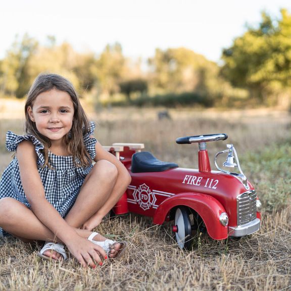 Mädchen sitzt im Gras neben einem roten Rutschauto