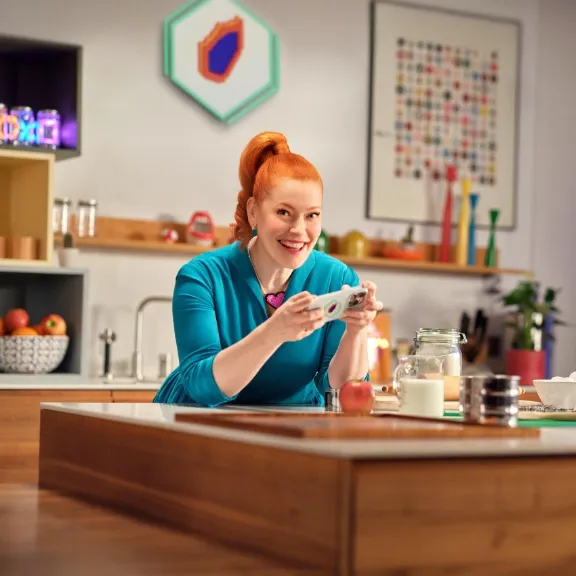 Enie steht in einer Küche und spielt auf einem Handy.