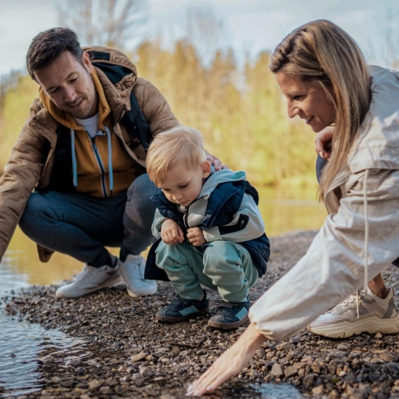Familie mit Kleinkind spielen am Rande eines Sees mit dem Wasser.