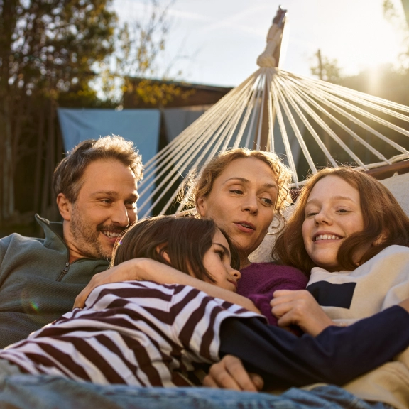 Eine Familie mit Vater, Mutter und zwei Kindern liegt vergnügt in einer Hängematte.