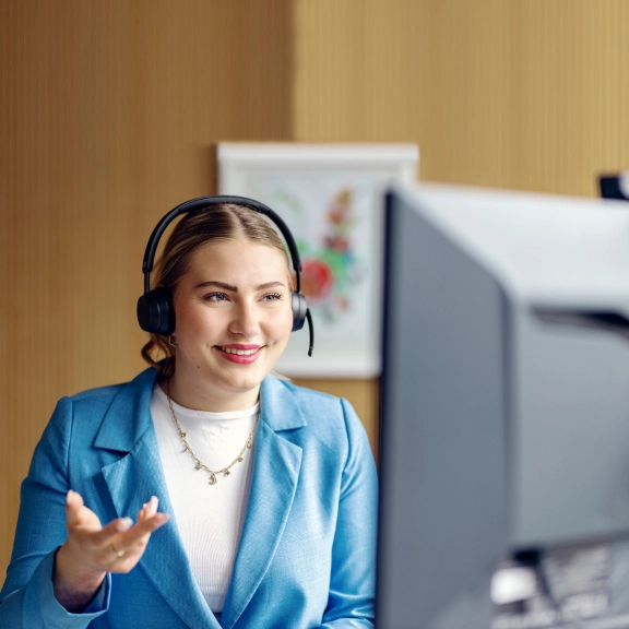 Junge Frau mit Headset vor einem Bildschirm in einer digitalen Beratungssituation.