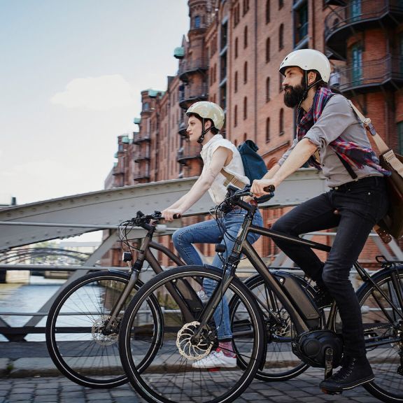 Zwei Personen fahren mit e-bike durch Stadt.