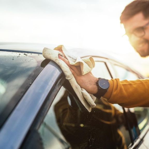 Autopflege im Frühjahr Junger Mann wischt das Dach seines Autos mit einem Mikrofasertuch sauber.