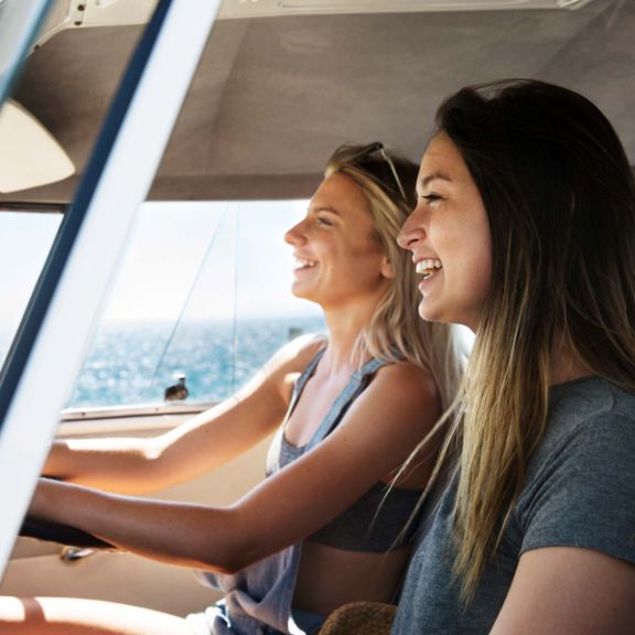 Zwei Frauen fahren mit dem Auto an der Küste entlang.