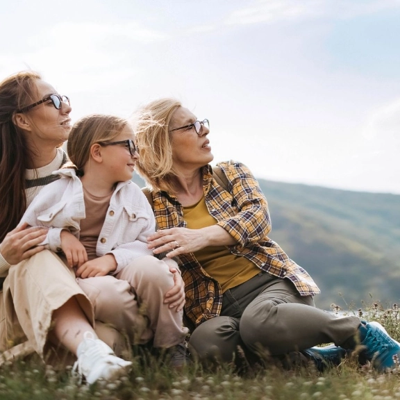 Drei Generationen sitzen zusammen in der Natur: Großmutter, Mutter und Tochter blicken zuversichtlich in die Zukunft..