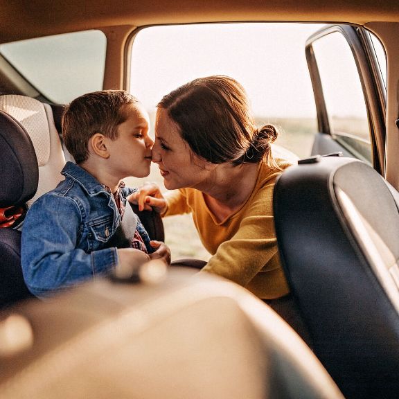Mutter und Kind Parkplatz Mutter schnallt ihren Sohn im Kindersitz an.