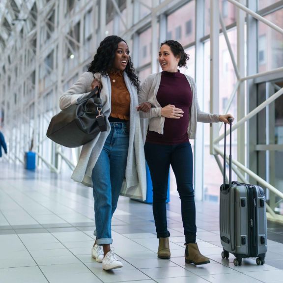 Zwei Frauen sind am Flughafen. Eine der Frauen ist schwanger.