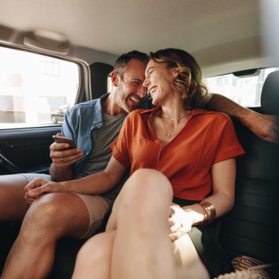 Mann und Frau lachen auf der Rückbank eines Autos.