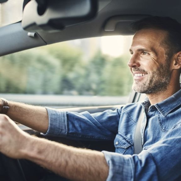 Mann sitzt fröhlich in seinem Auto.