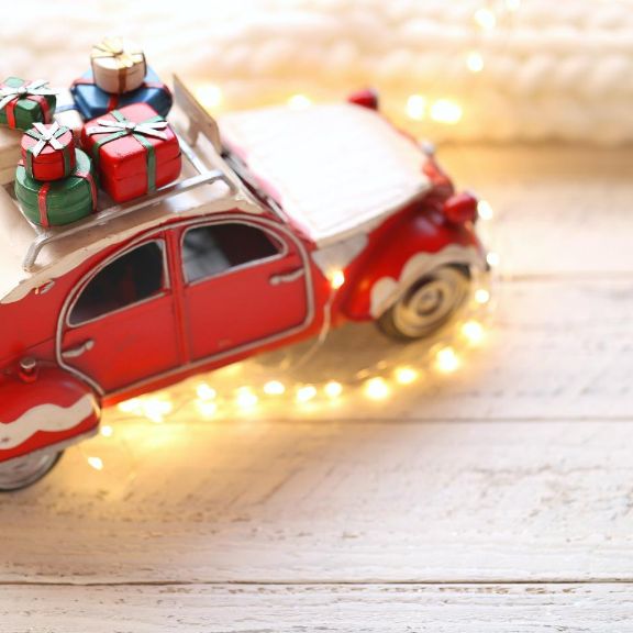 Weihnachtsauto mit Geschenken, Lichterkette und weißem Strickschal im Hintergrund.