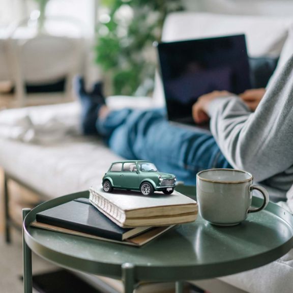 Person sitzt mit Kaffee und Laptop auf dem Sofa.