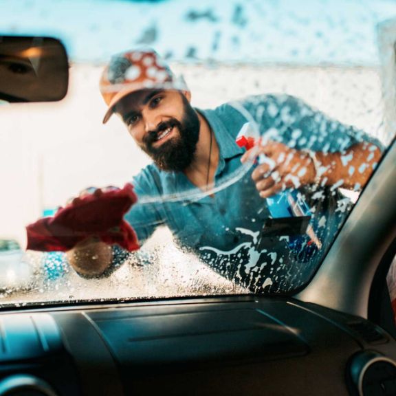 Auto selbst waschen Mann wischt die Frontscheibe seines Autos ab.