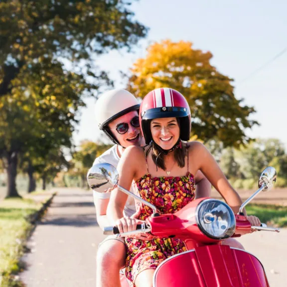 Junge Frau sitzt auf Ihrer Vespa, schließt Ihren Helm und denkt mit Freude, dass Sie mit dem Moped gut versichert ist.