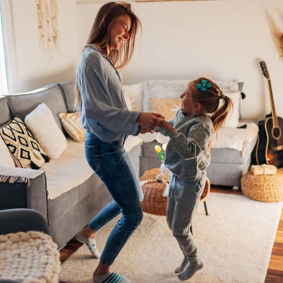 Mutter und Tochter springen gemeinsam im Wohnzimmer.
