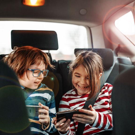 Geschwister spielen am Smartphone im Auto.