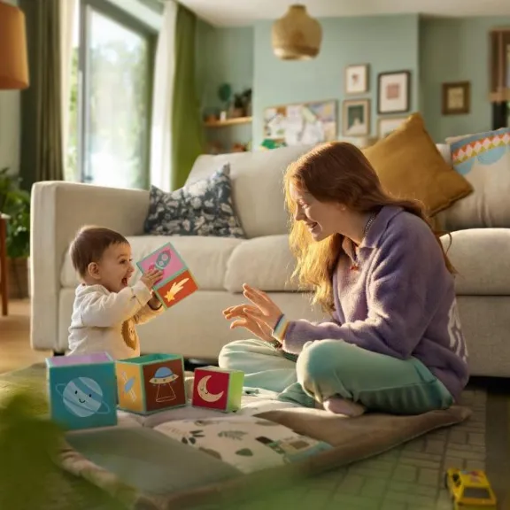 Zwei Geschwister spielen auf einem Teppich miteinander.