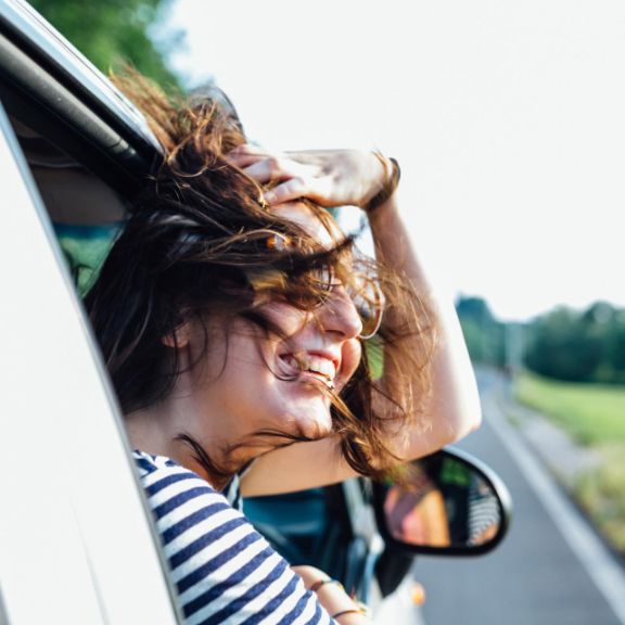 Frau lehnt den Kopf während der Fahrt aus dem Auto.