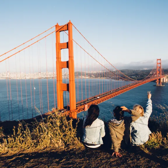 3 junge Leute genießen die Aussicht auf die Golden Gate Bridge bei Ihrem Urlaub in den USA.