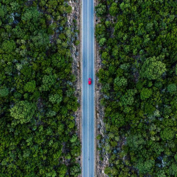 CO2-Austoß Luftaufnahme eines roten Autos, entlang einer Straße, flankiert durch einen grünen Wald.