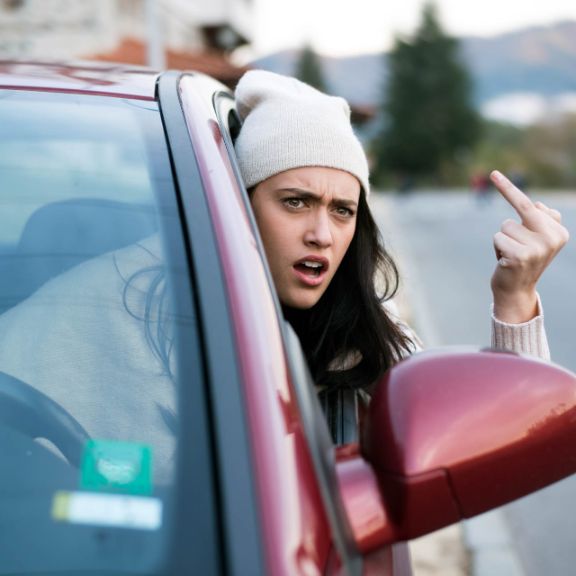 Beleidigungen im Straßenverkehr Frau macht rüde Geste im Auto.