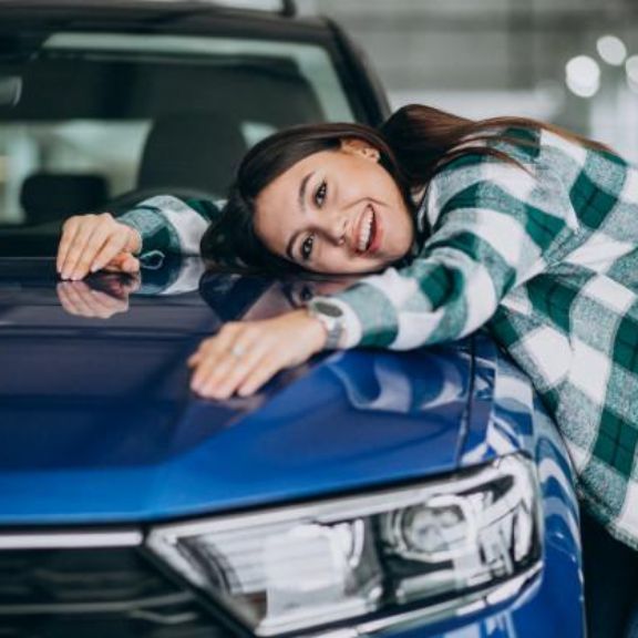 Junge Frau umarmt die Motorhaube eines blauen Autos