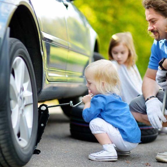 Vater und Kinder pruefen Reifendruck.