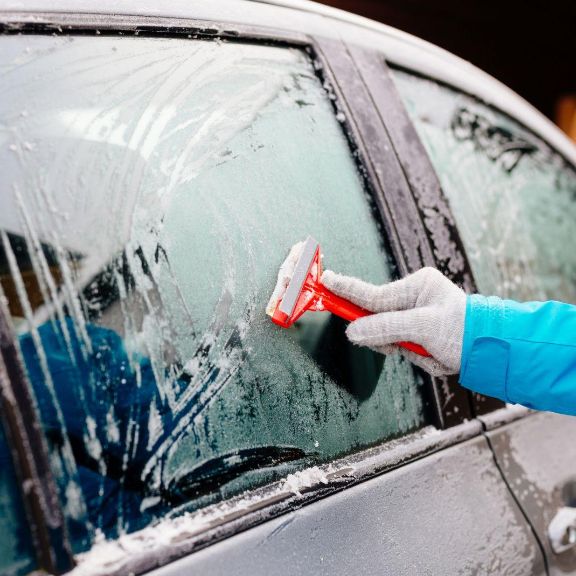 Person enteist Autoscheibe mit Eiskratzer.