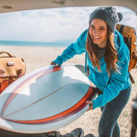 Frau packt ein Surfbrett in den Kofferraum.