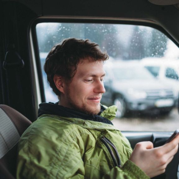 Junger Mann sitzt im Auto und blickt auf sein Handy.