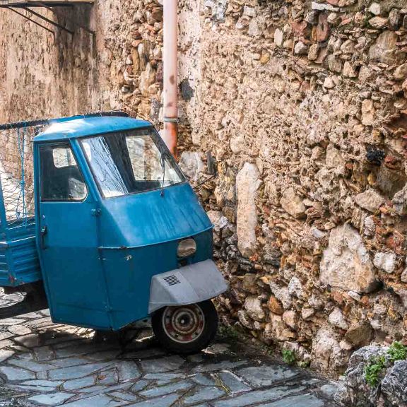 Leichtfahrzeuge Italienische Ape Piaggio parkt an Steinmauer.