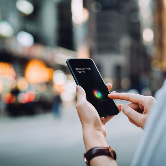 Person hält Smartphone in der Hand und benutzt Sprachassistenten.